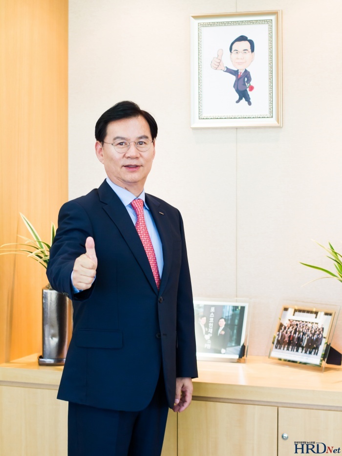 박귀찬 원장이 직원이 그려준 자신의 캐리커처가 걸려 있는 집무실 벽 앞에서 같은 포즈를 취하고 있다.